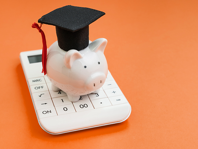 Piggy bank with grad cap sitting on white calculator infront of orange background